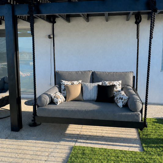 Gray swing with patterned cushions on a patio area with grass and a wall in the background.
