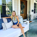 Woman sitting on a white outdoor swing bed with blue and white pillows, smiling at the camera.