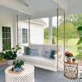 White swing bed with blue and patterned cushions on a decorated porch.