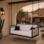 Outdoor swing with white cushions and black metal frame in a desert-themed patio setting.