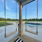 Wooden swings hanging from a porch with a pool and garden view.
